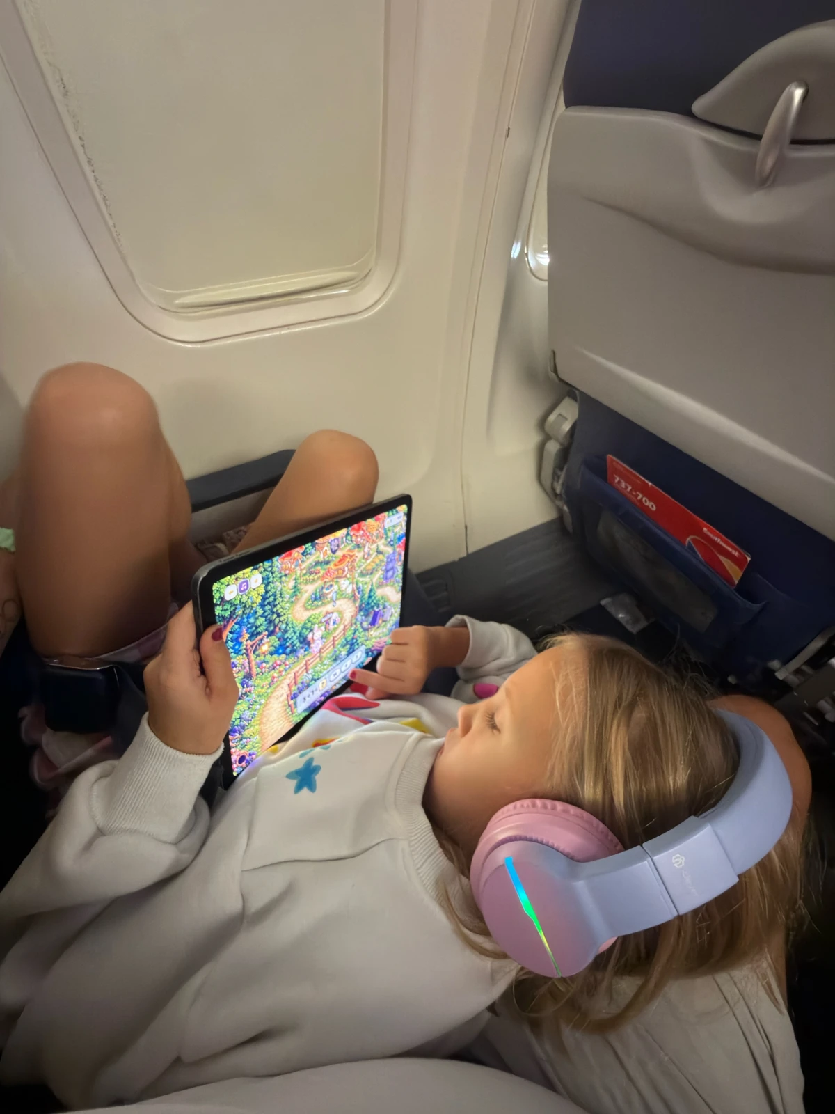 Brooklyn playing Bella and Pan on an iPad during a flight, wearing headphones.